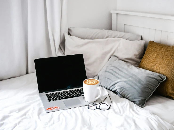 a laptop on a bed with a cup of coffee