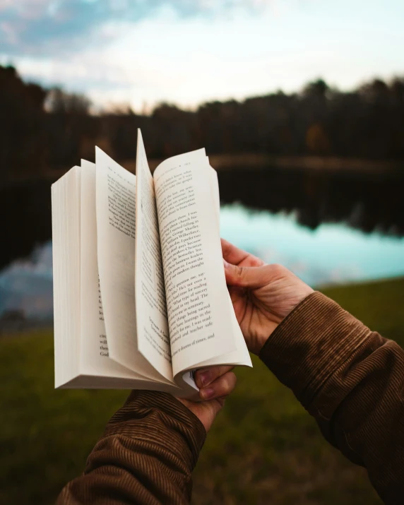 a person is holding an open book in the grass