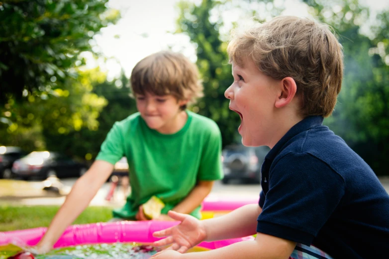 a boy in green shirt and another boy in blue t - shirt sit on float with water