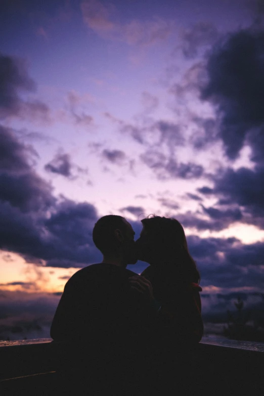 two people kissing against a purple sky