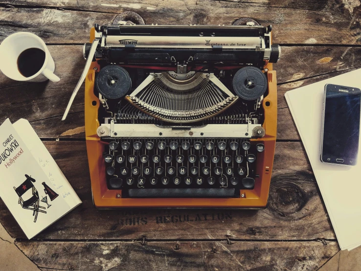 an old fashioned typewriter next to a cup of coffee and paperwork on a table