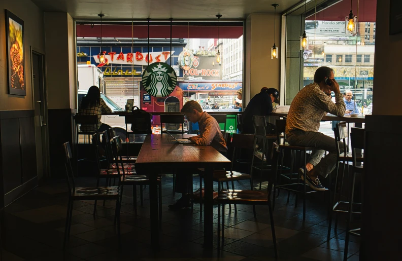 a couple sitting at tables in a restaurant eating and looking into the window