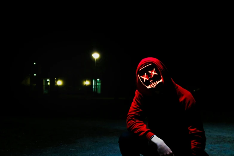 man in hooded red cloth crouching against camera
