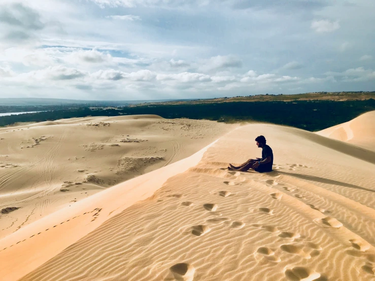 man sitting alone in a sand dune while looking at the ocean