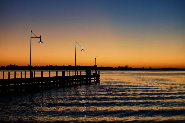 the sun is setting over the water by the pier