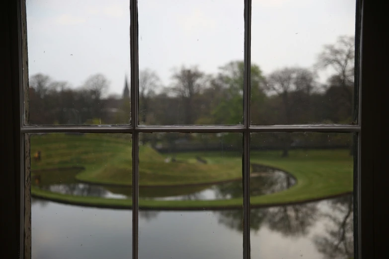 a view out of a window into a large garden with water and trees