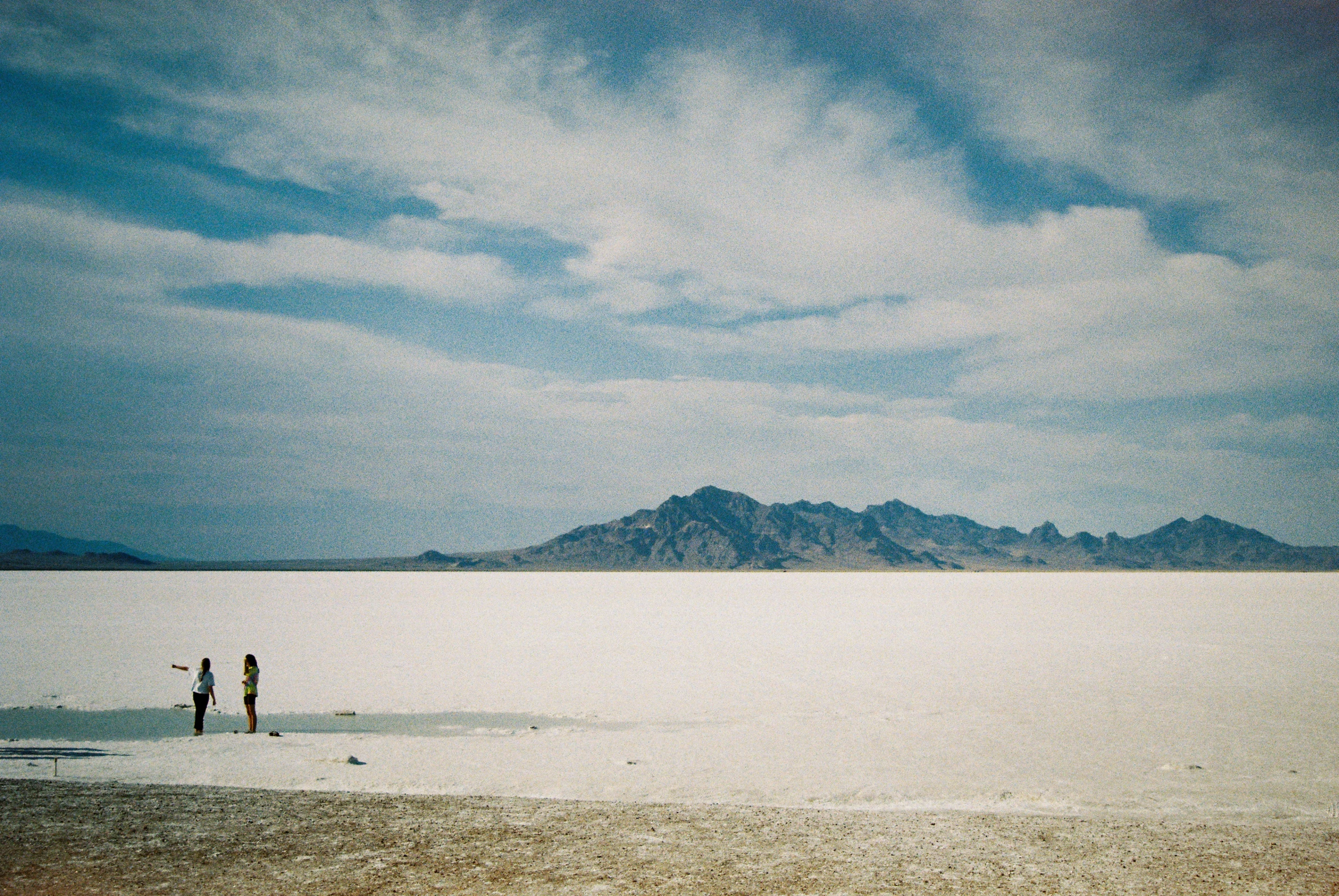 two people standing on a body of water near mountains