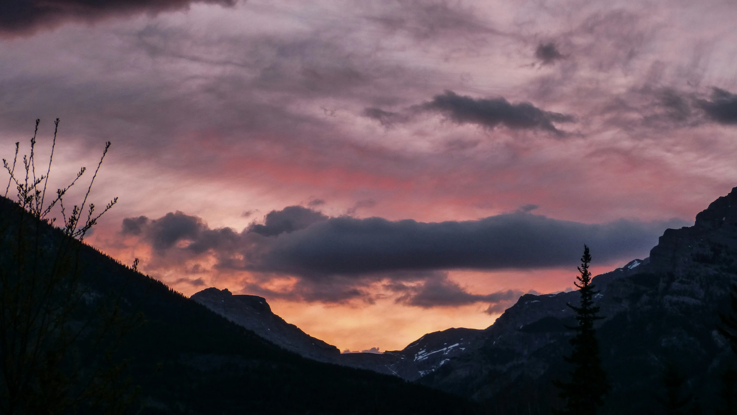 the sun sets in front of mountains with trees