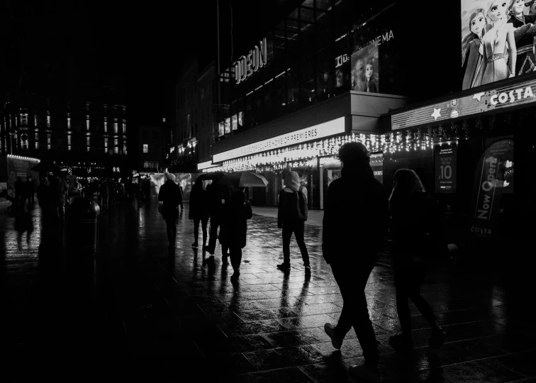 people walking down a sidewalk at night in the rain