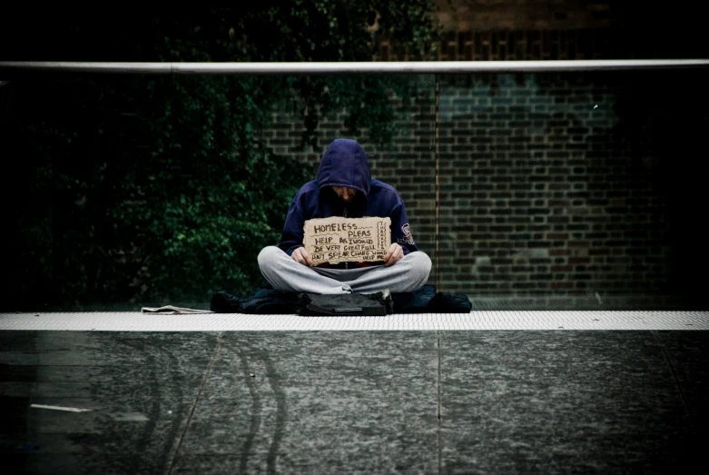 a man sitting on the ground holding a sign