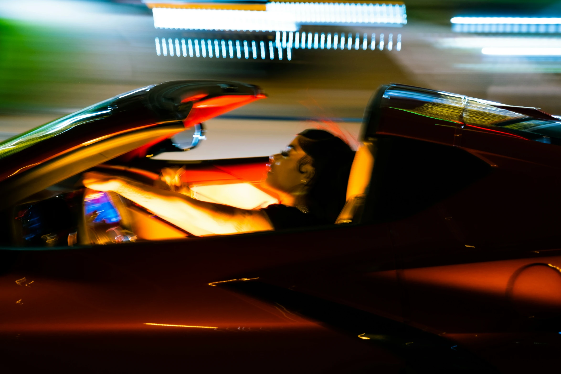 a woman sitting in the driver's seat of a red car at night