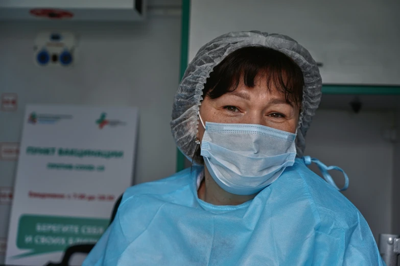 a woman in scrubs stands in an operating room wearing a surgical mask