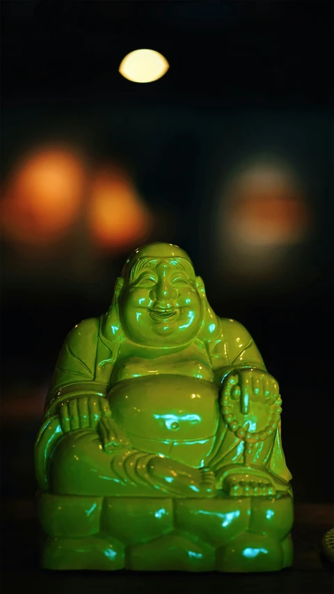 a green lit buddha figurine with eyes closed and a candle in the background