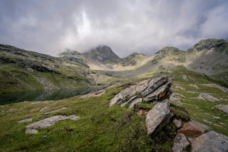 some mountain side rocks water grass and clouds