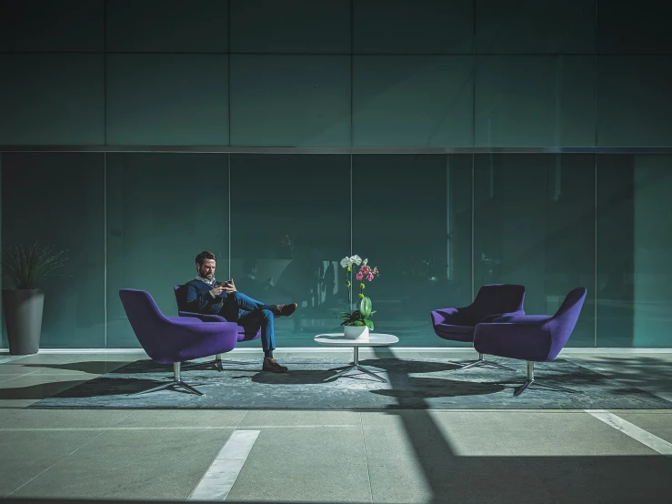 two men sit in purple chairs while a man stands behind them