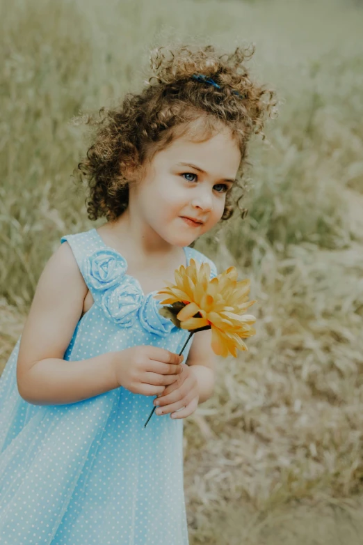 an adorable little girl in blue holding a flower