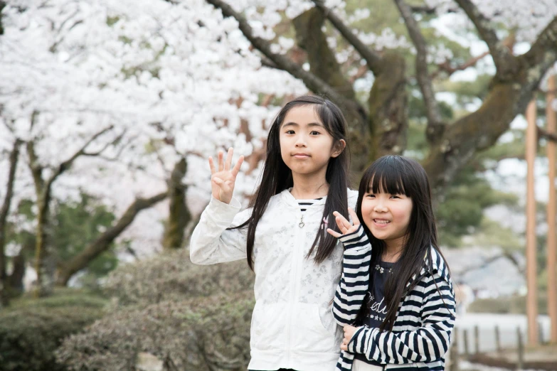 two girls are standing on the side walk, waving