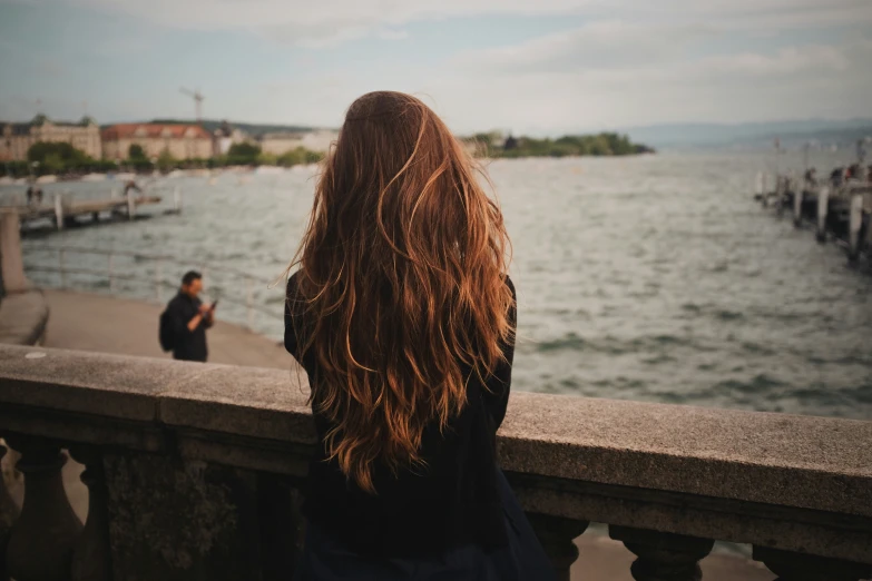 a woman walking along side a river next to a fence