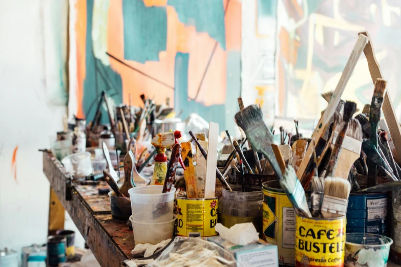 a table with many paints, brushes and some empty cans