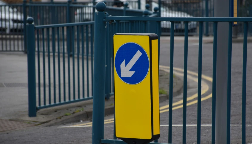 yellow sign standing beside a fence with an arrow pointing upward