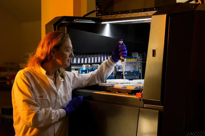 a woman in white lab coat and blue gloves working on machine