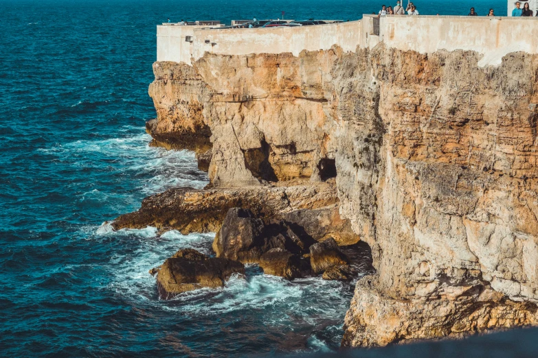 a group of people stand on the top of a cliff next to the ocean