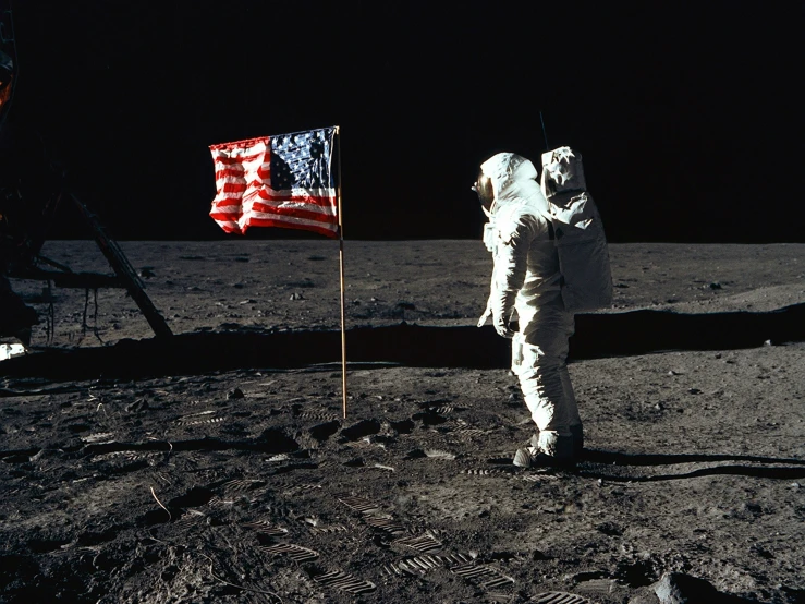 an astronaut in white standing on the moon next to a american flag