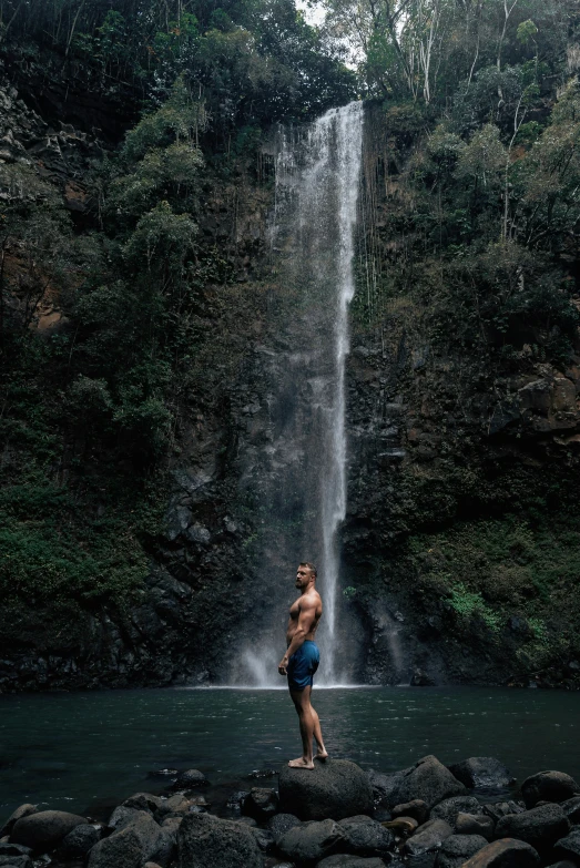 the man is standing in front of a tall waterfall