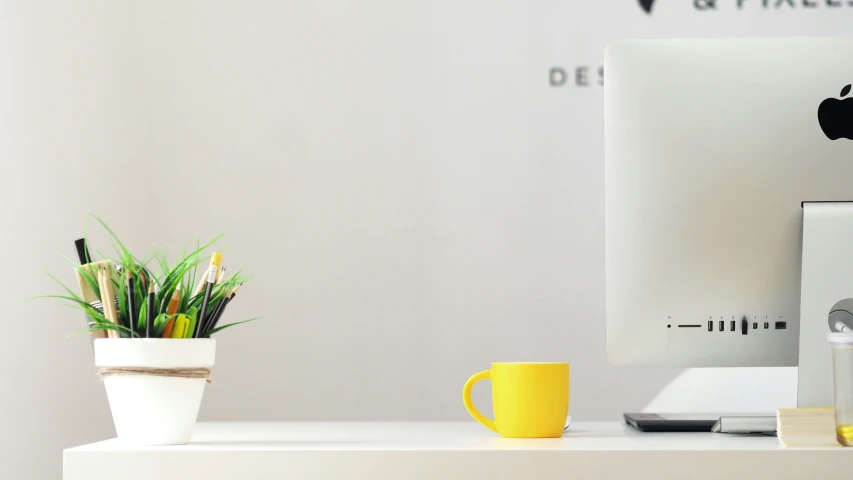 an apple desktop computer and a yellow mug on a desk