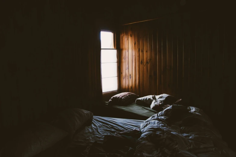 an unmade bed with the sunlight through two windows