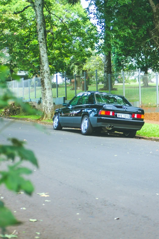 black sports sedan with chrome rear bumpers driving along a residential street