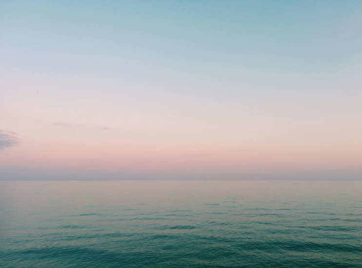 an empty sea at dusk with an airplane flying above the horizon