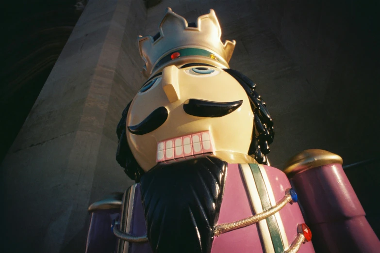 the mask statue is wearing a golden crown and carrying a purple suitcase