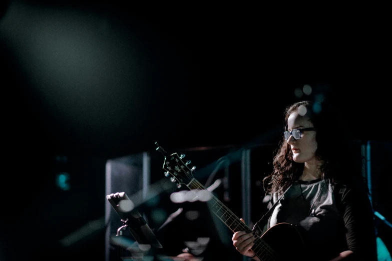 a girl playing guitar on stage while staring back