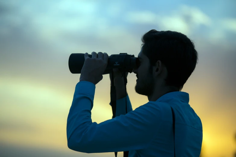 man in a blue jacket looking into the sky through binoculars