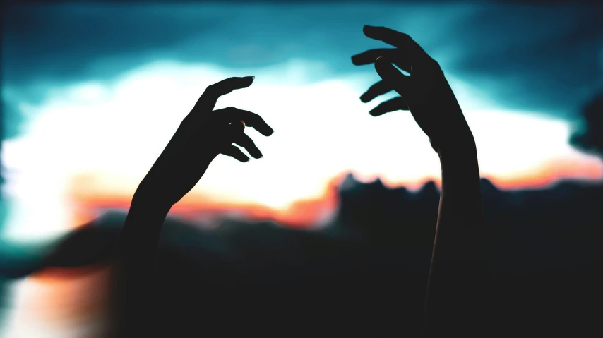 silhouette of two hands reaching up in front of a sunset