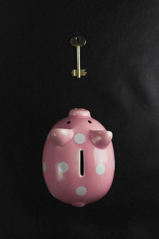 a small pink pig shaped piggy bank with a golden key hanging from it's center