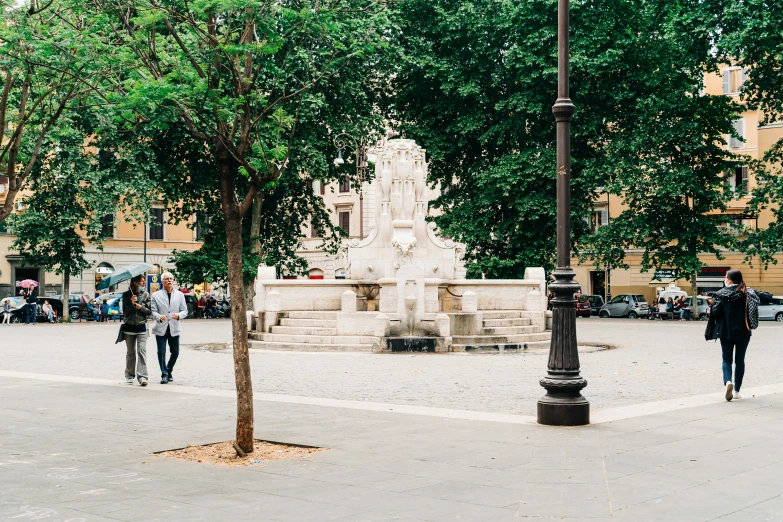 two people walking past a fountain in the middle of a street