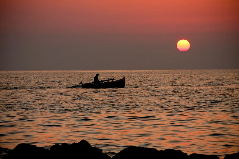 boat in the ocean during sunset or sunrise with silhouette of man sitting on edge