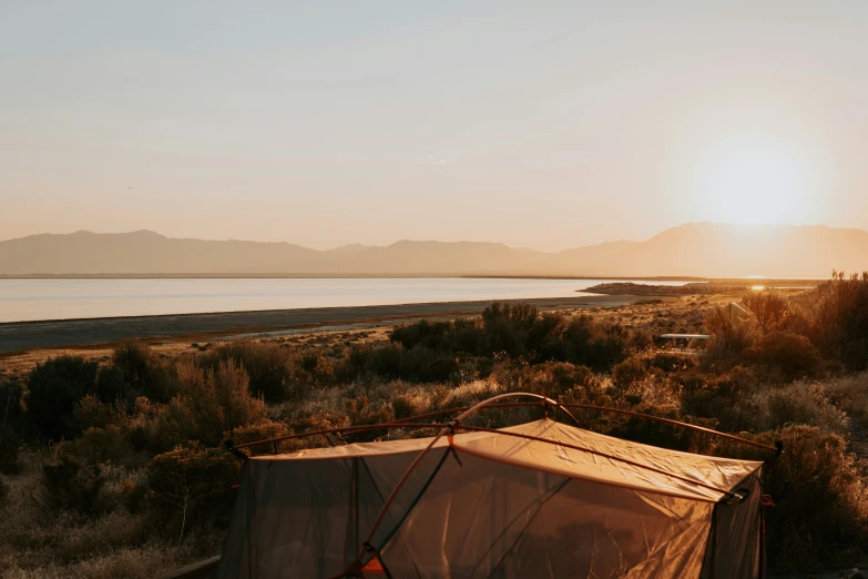 tent on dirt field near body of water during sunrise