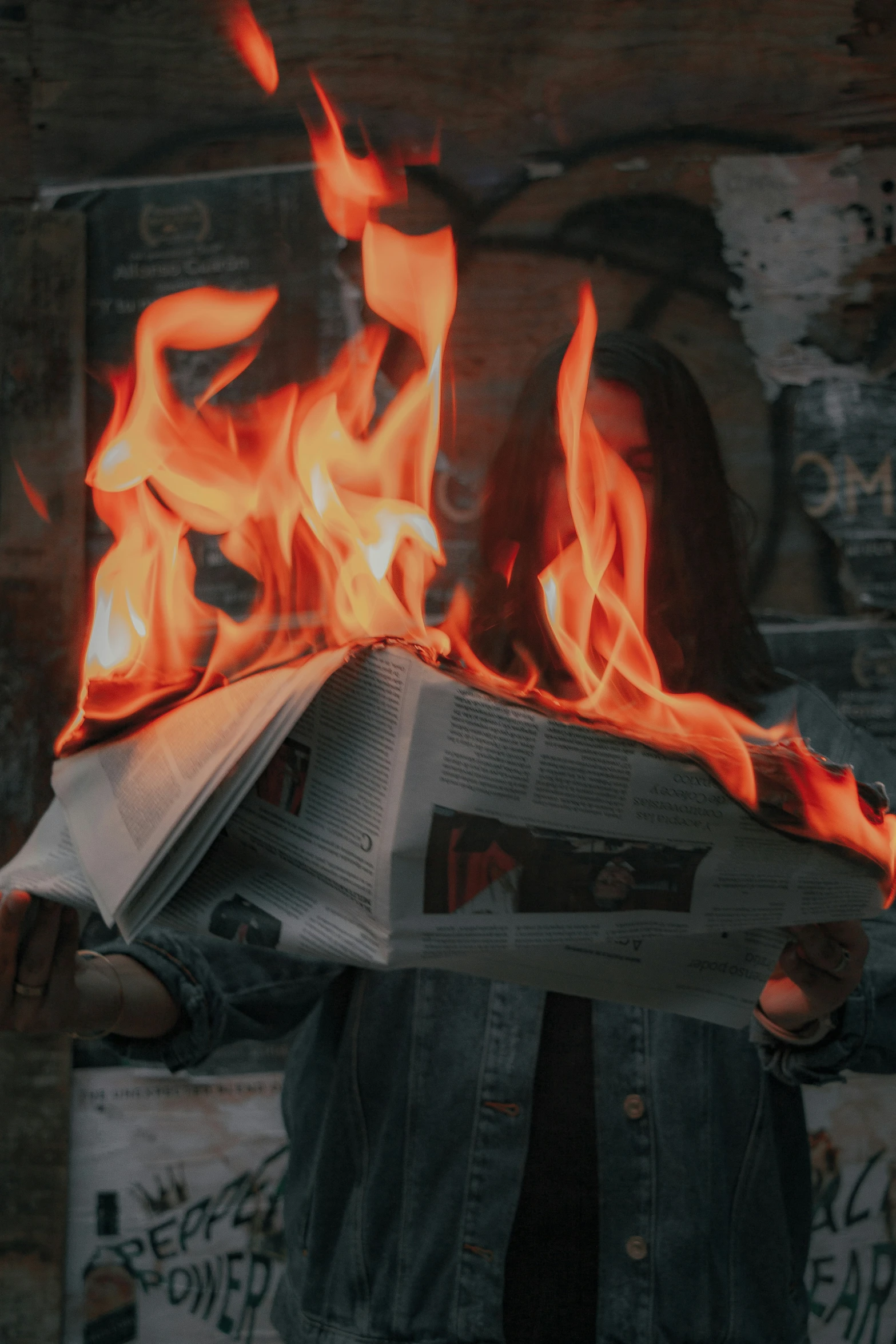 person wearing jeans and jacket holding a newspaper with flames on it