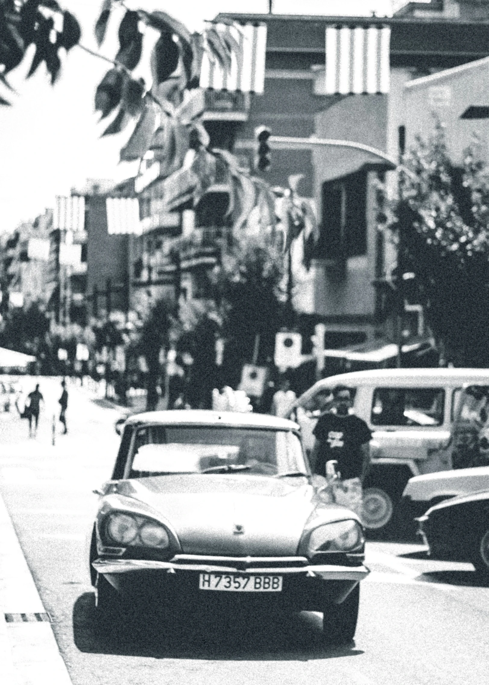 black and white pograph of cars and people walking in a busy street