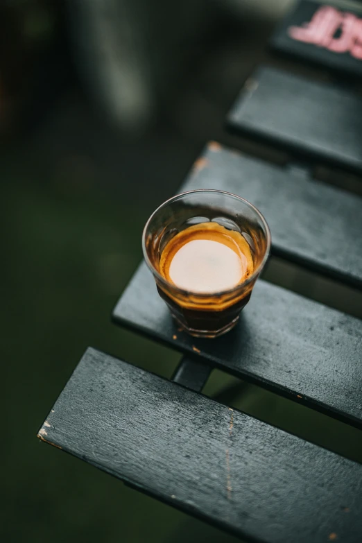 a glass with liquid sitting on a wooden bench