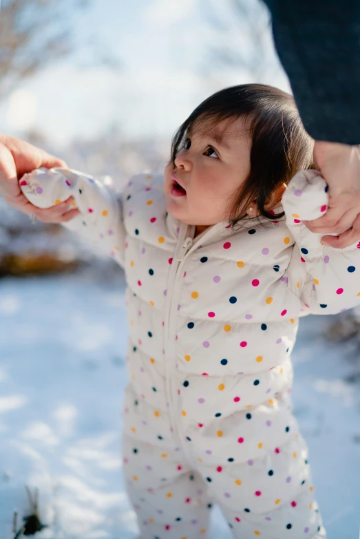 small baby standing in snow holding onto parent's hand