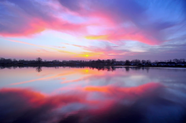 the sun sets over a river and reflecting in the water