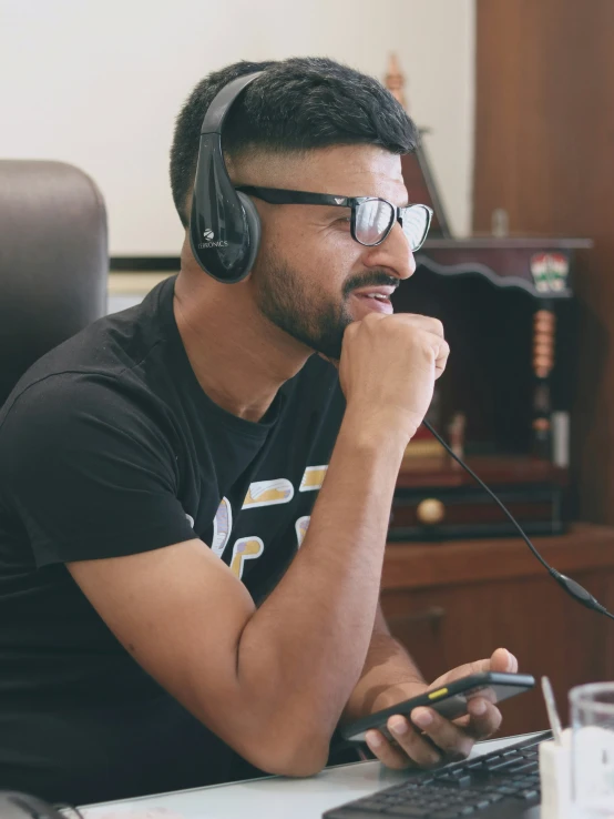 a man in glasses and headphones sitting at his desk