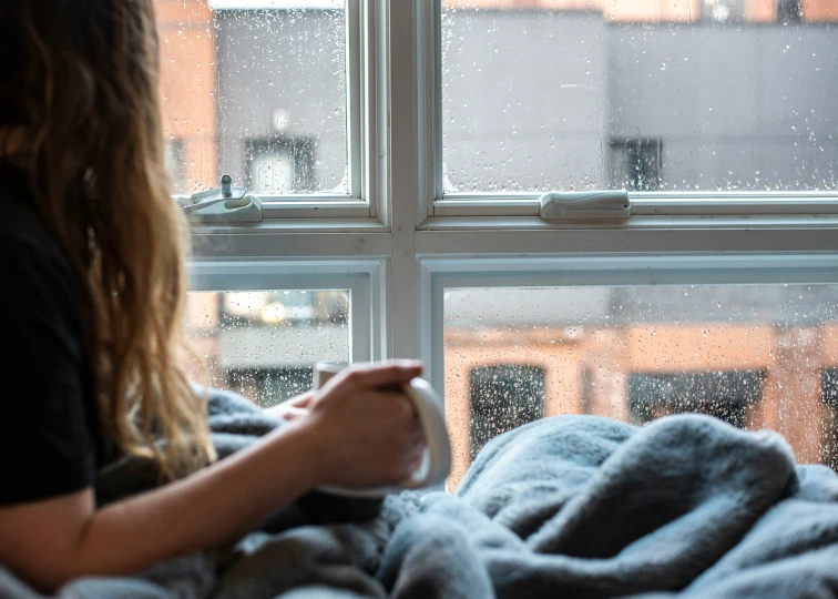 a woman sitting on her bed while looking out the window