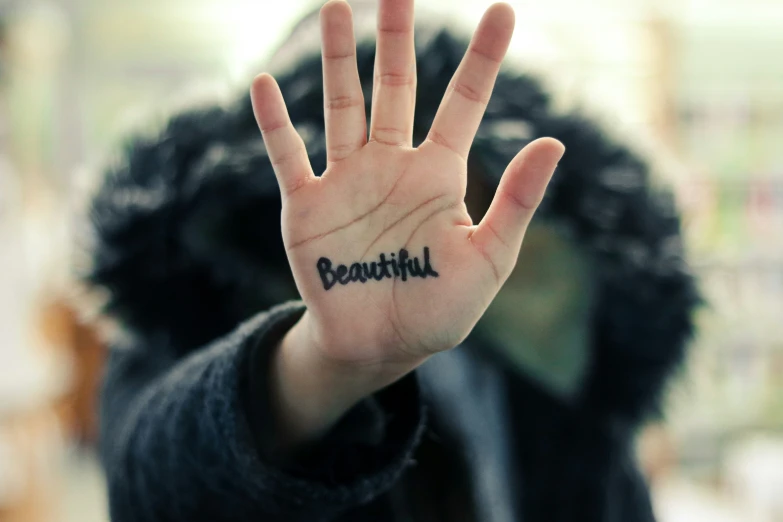 the person holds their hand up with the word beautiful tattooed on it