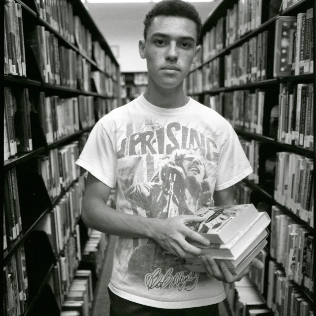 young man holding book standing between rows of books