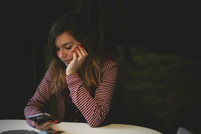 the woman looks at her phone while sitting in a dark place